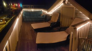 A balcony with two lounge chairs and a sofa, wooden railings, and a view of parked cars. - A Sandcrab & Jellyfish Walk Into a Sand-Bar (Ocean City)