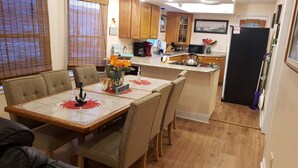 A dining area with a table set for four, a kitchen in the background, wooden cabinets, and a refrigerator. - A Sandcrab & Jellyfish Walk Into a Sand-Bar (Ocean City)