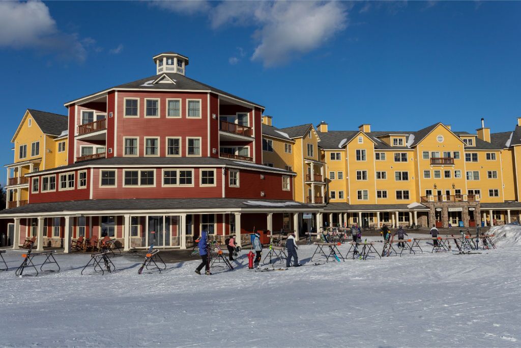 A multi-story hotel with a red and yellow facade, ski equipment in the foreground, and a clear blue sky.