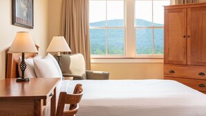 Ein Hotelzimmer mit Bett, Schreibtisch, Stuhl, Lampe, Kleiderschrank und einem Fenster mit Blick auf die Berge.