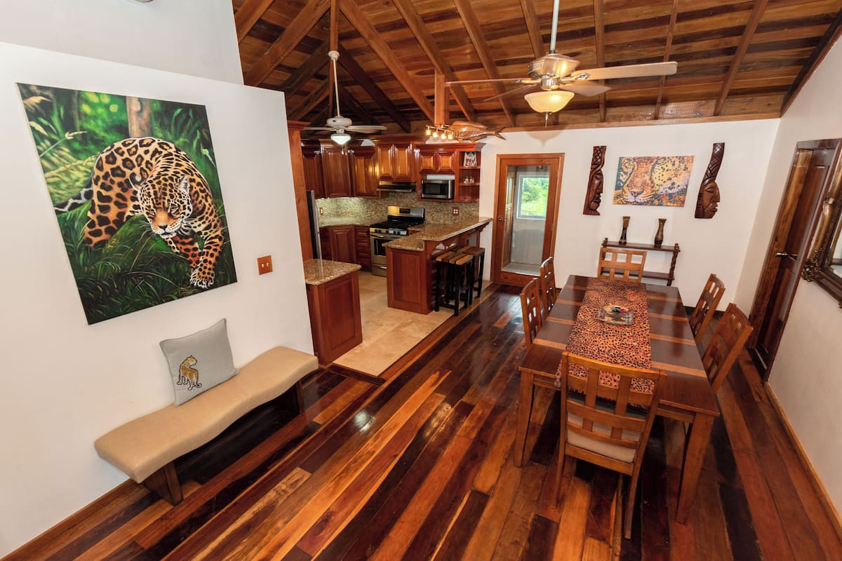 A spacious kitchen with wooden cabinets, a dining area with a long table and chairs, a bench, and a ceiling fan.