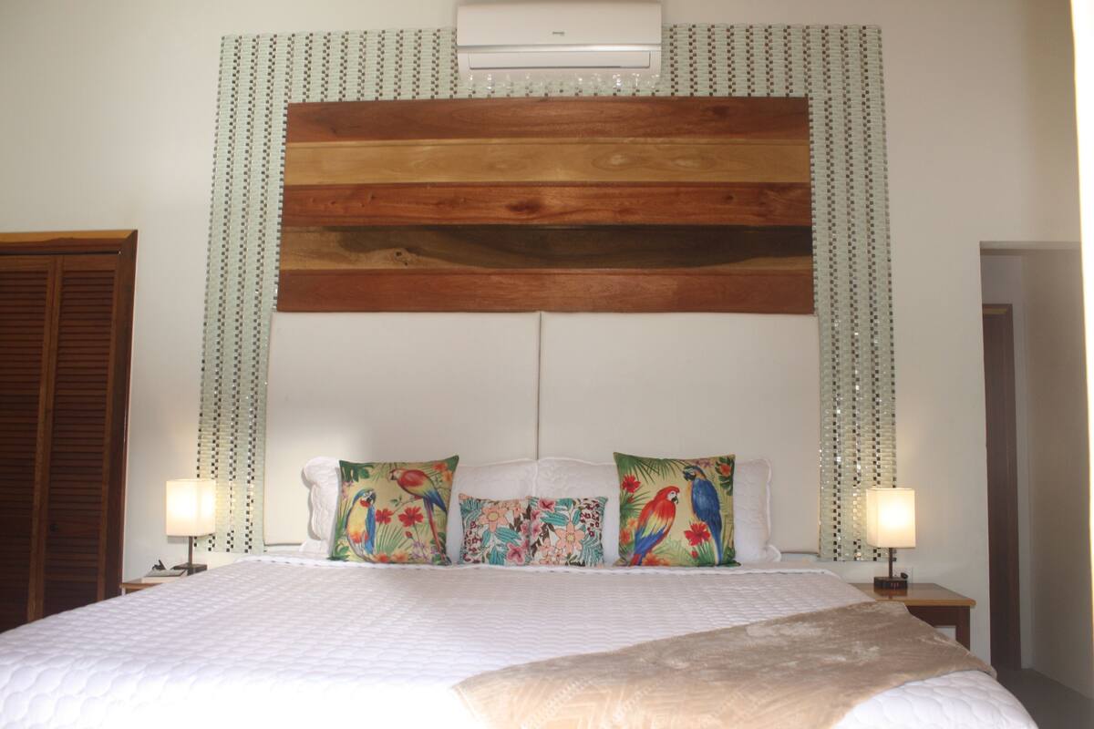 A hotel room with a large bed, two nightstands with lamps, a wooden headboard, and decorative pillows.