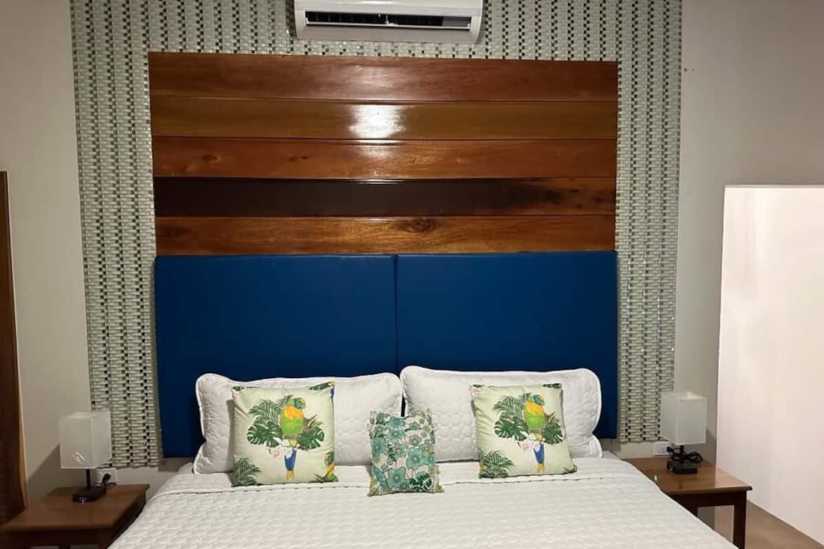 A hotel room with a wooden headboard, white bedding, and tropical-themed pillows.