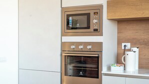 A compact kitchen with a microwave, oven, and a coffee maker on a counter. - Villa Celestina (Marco Simone)