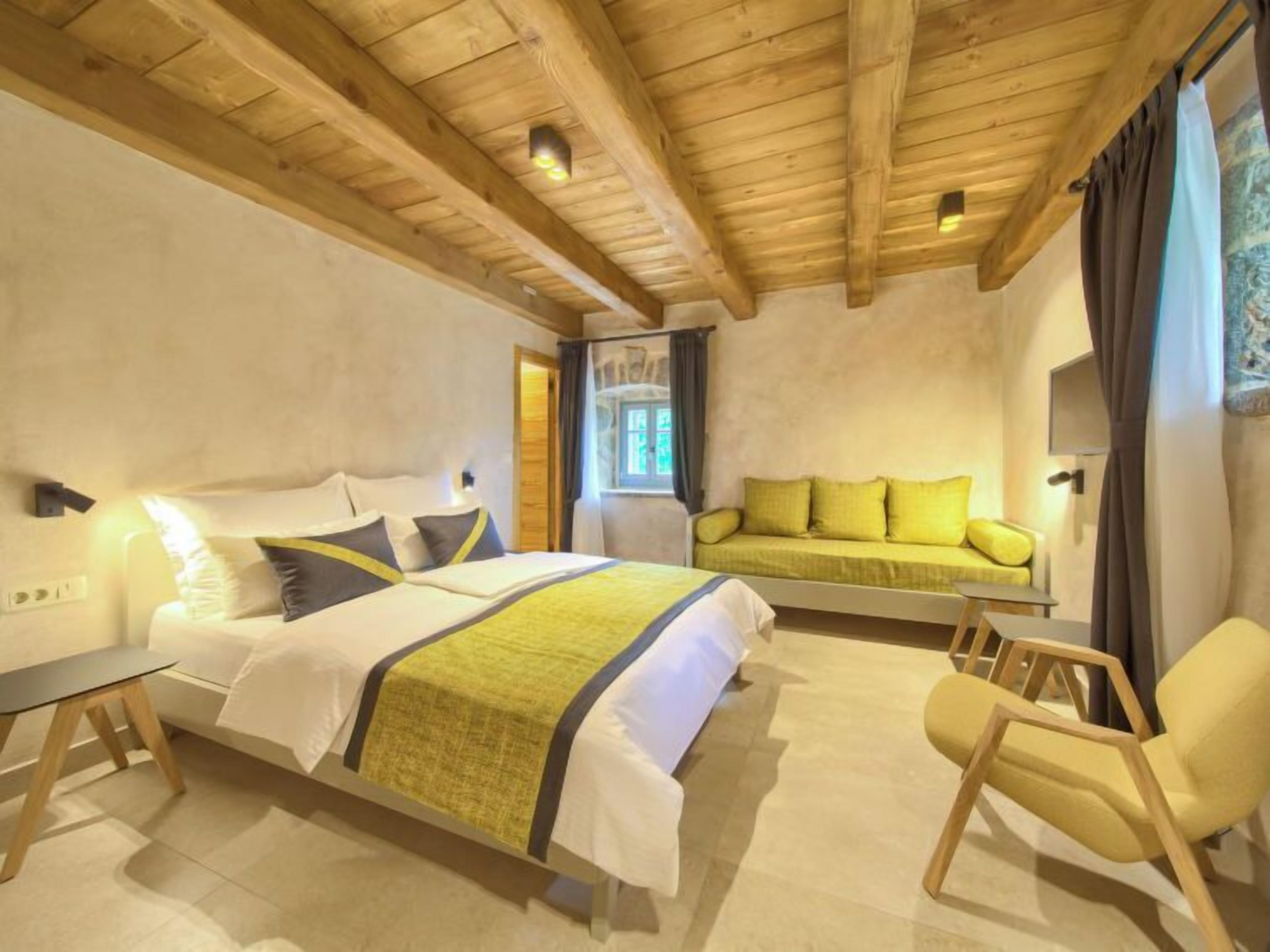 A bedroom with a bed, a sofa, a chair, and a window with curtains.