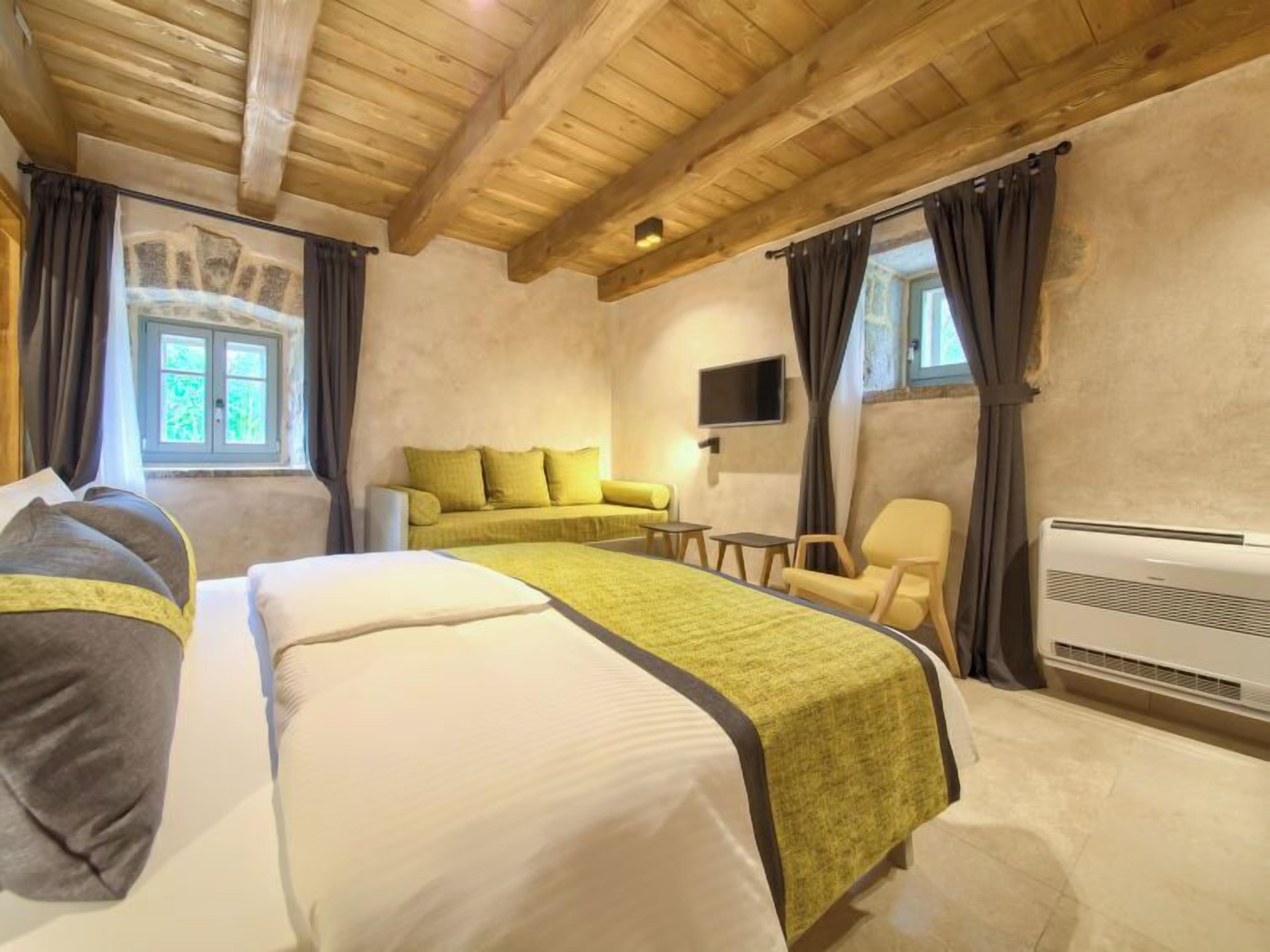 Une chambre d’hôtel avec un plafond en bois, un lit recouvert d’une couverture verte, un canapé, une chaise, un téléviseur et un appareil de climatisation.