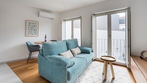 A modern living room with a teal sofa, a small round table, and a dining area with a chair and a table. - GuestReady -  Downtown refuge with charm (Porto)