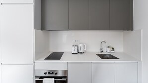 A modern kitchen with white cabinets, a double sink, a built-in oven, and a coffee maker. - GuestReady -  Downtown refuge with charm (Porto)