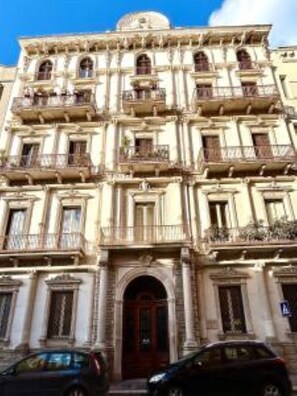 Un immeuble à plusieurs étages, doté d’une façade symétrique, de nombreux balcons et d’une entrée centrale avec une porte de couleur foncée.