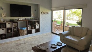 A living room with a beige sofa, a coffee table, a TV mounted on the wall, and a sliding glass door leading to an outdoor patio. - Amplio Depa en San José del Cabo, Zona Hotelera, Hasta 8 Personas, Alberca (San José del Cabo)