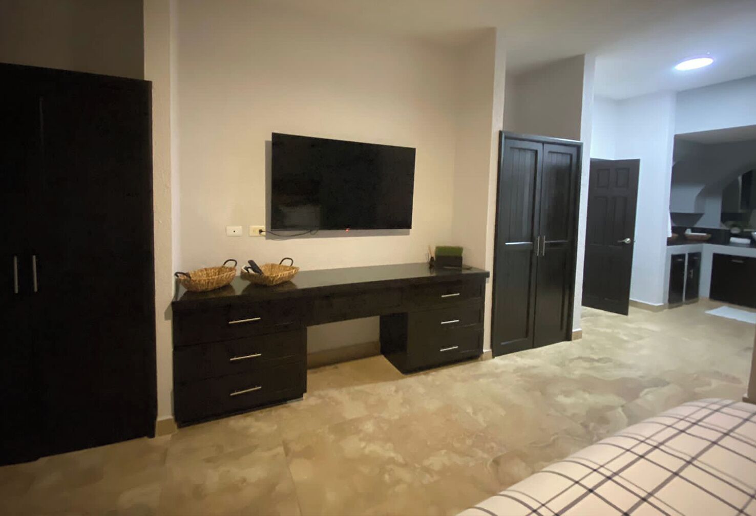 A bedroom with a bed, a desk with drawers, a television on the wall, and a wardrobe.