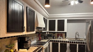 A kitchen with dark wooden cabinets, a stove, a sink, and a refrigerator. - Amplio Depa en San José del Cabo, Zona Hotelera, Hasta 8 Personas, Alberca (San José del Cabo)