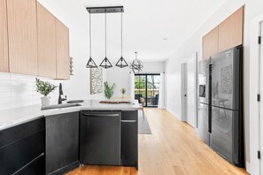 Une cuisine moderne avec des appareils électroménagers noirs, des meubles en bois et des luminaires suspendus.
