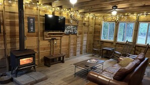 Un interior de cabaña acogedor con chimenea, paredes de madera, un sofá de cuero y un televisor.