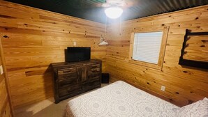 Habitación con paneles de madera, una cama, cómoda, televisor y ventana.
