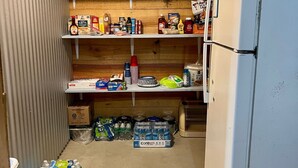 Una cocina compacta con refrigerador, estantes llenos de alimentos y una licuadora.