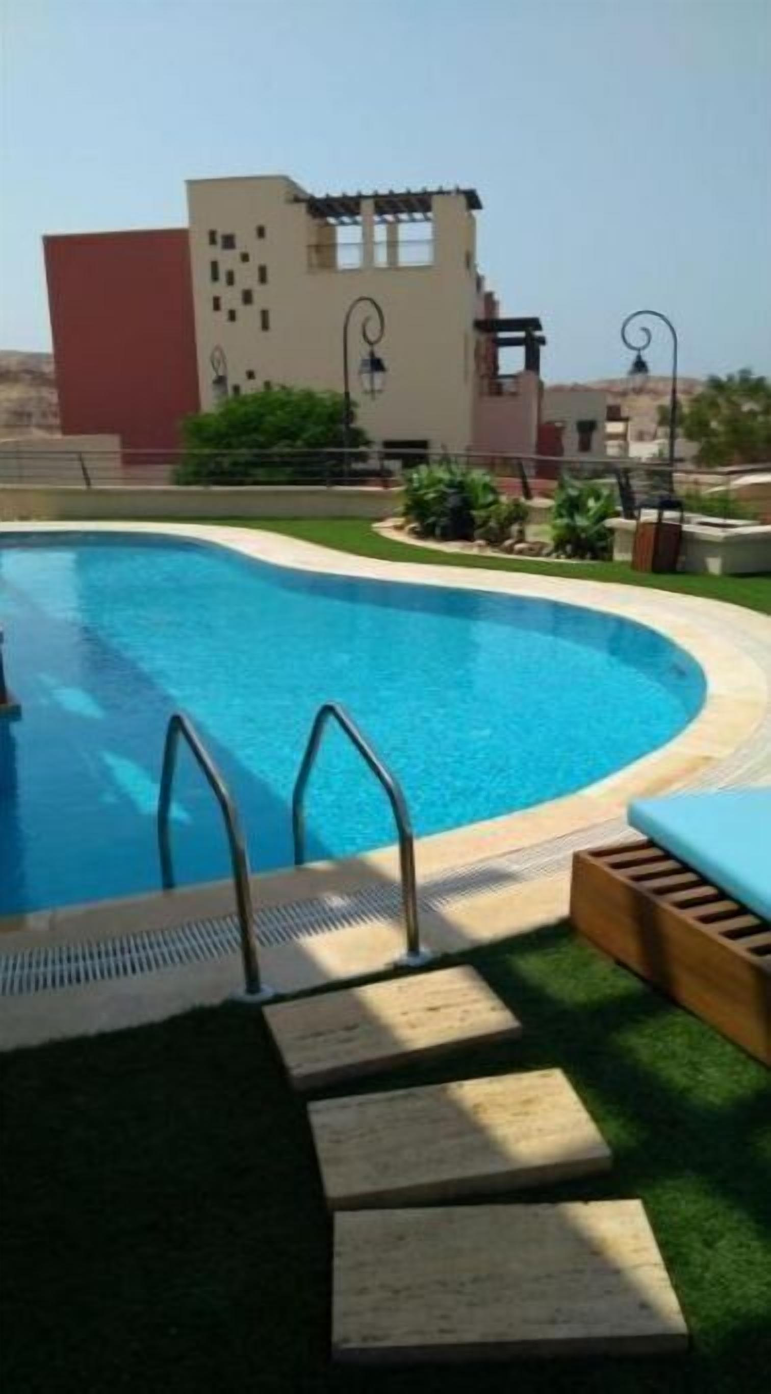 A swimming pool with steps leading into it, surrounded by a grassy area and a building in the background.