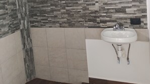 Une salle de bain avec une douche, des murs carrelés, un lavabo et un plancher en bois.