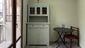 A room with a light green wall, a white cabinet with glass doors, a small round table with a red cushion, and a chair. - 35 Arsena St (Tbilisi)