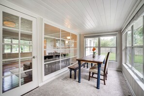Enjoy a spacious room with a high ceiling, sliding glass door to an outdoor area and a wooden dining table.