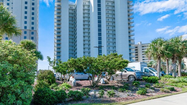 A high-rise hotel with multiple floors, surrounded by lush greenery and palm trees. - Palacio 1702 | Beachfront, Resort Amenities | My Beach Getaways (Pensacola)