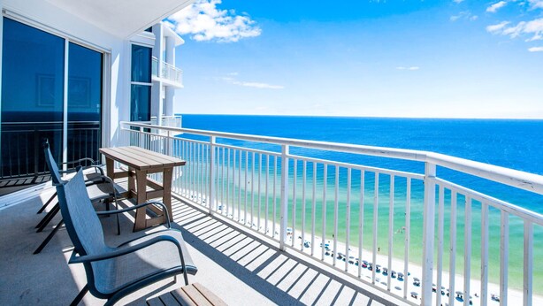 Un balcon avec vue sur l’océan, une table en bois et deux chaises.