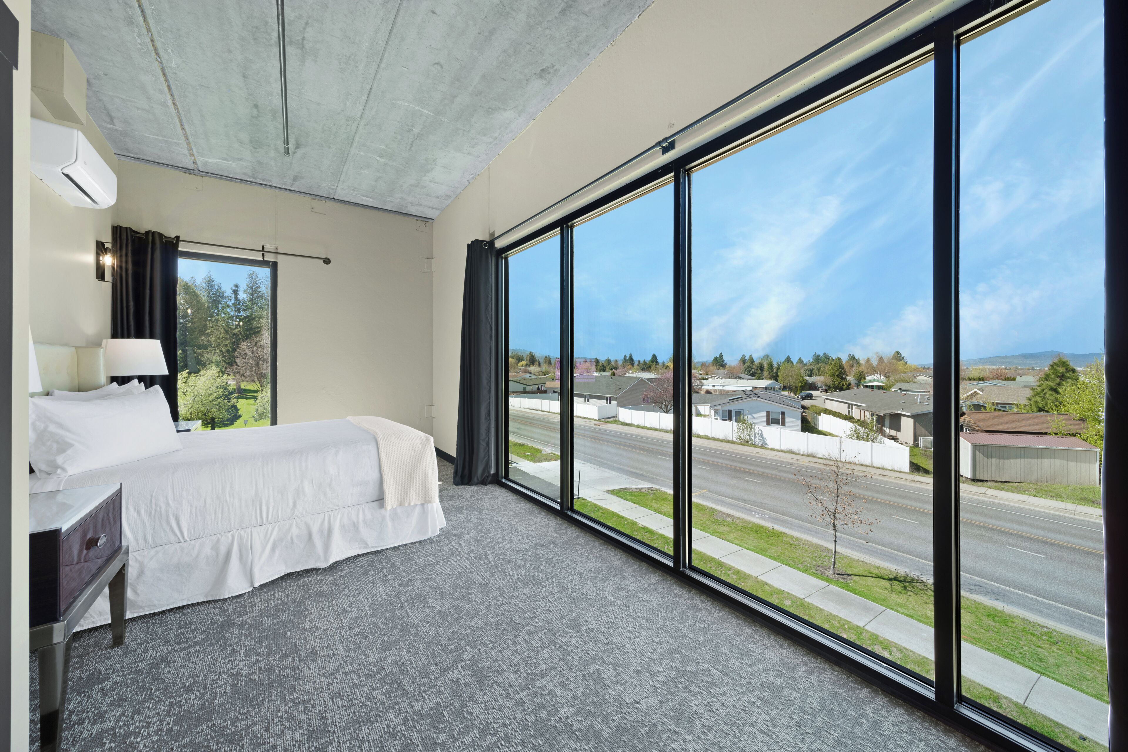 A hotel room with a large window, a bed, a desk, and a lamp.