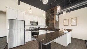 A modern kitchen with white cabinetry, stainless steel appliances, a central island, and pendant lighting. - The Suites at Prairie Falls & Event Center (Post Falls)