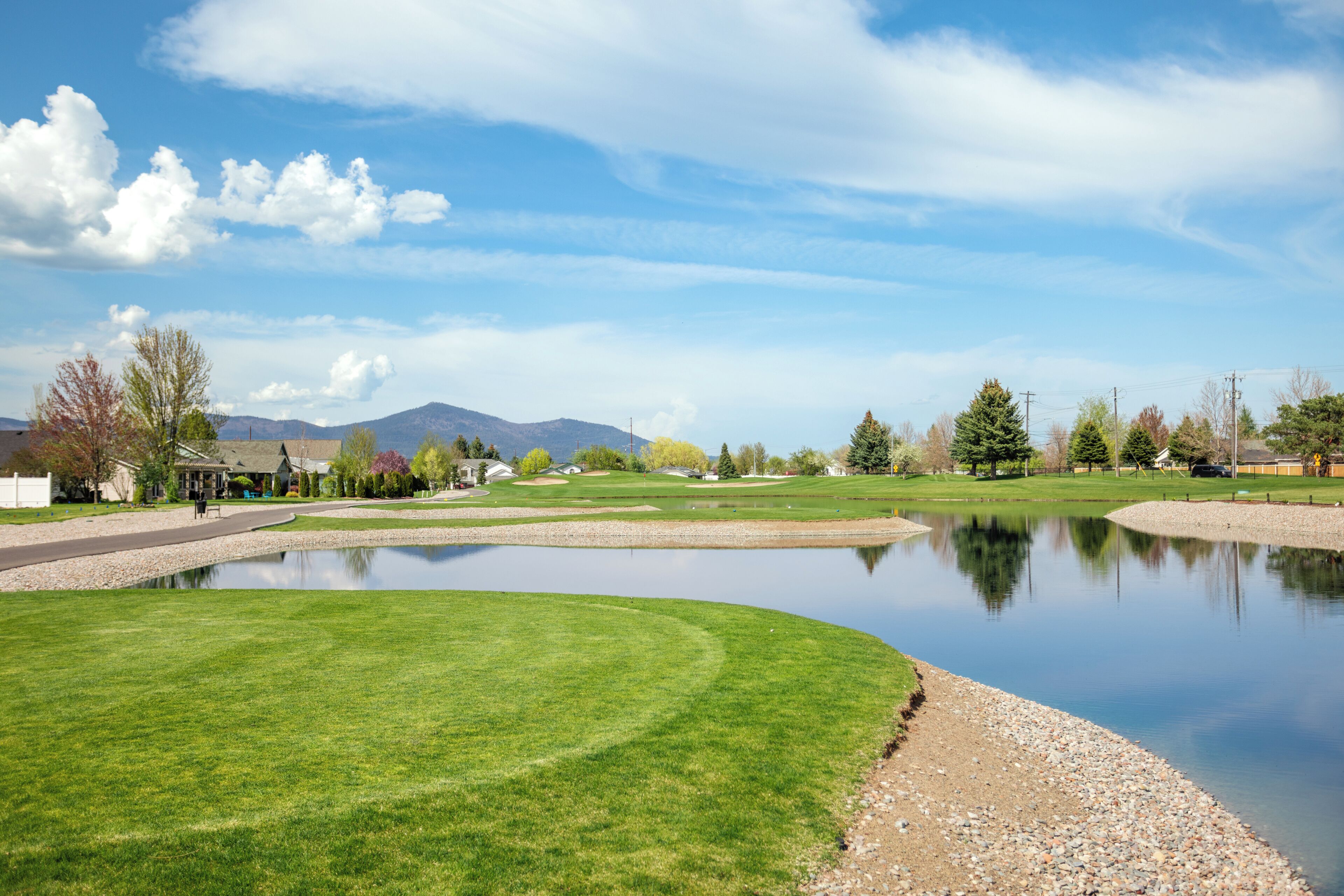 A golf course with a pond, houses, and mountains in the background.