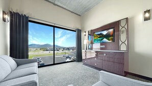 A hotel room with a large sliding glass door leading to a parking area, a flat-screen TV mounted on the wall, and a small cabinet with drawers. - The Suites at Prairie Falls & Event Center (Post Falls)
