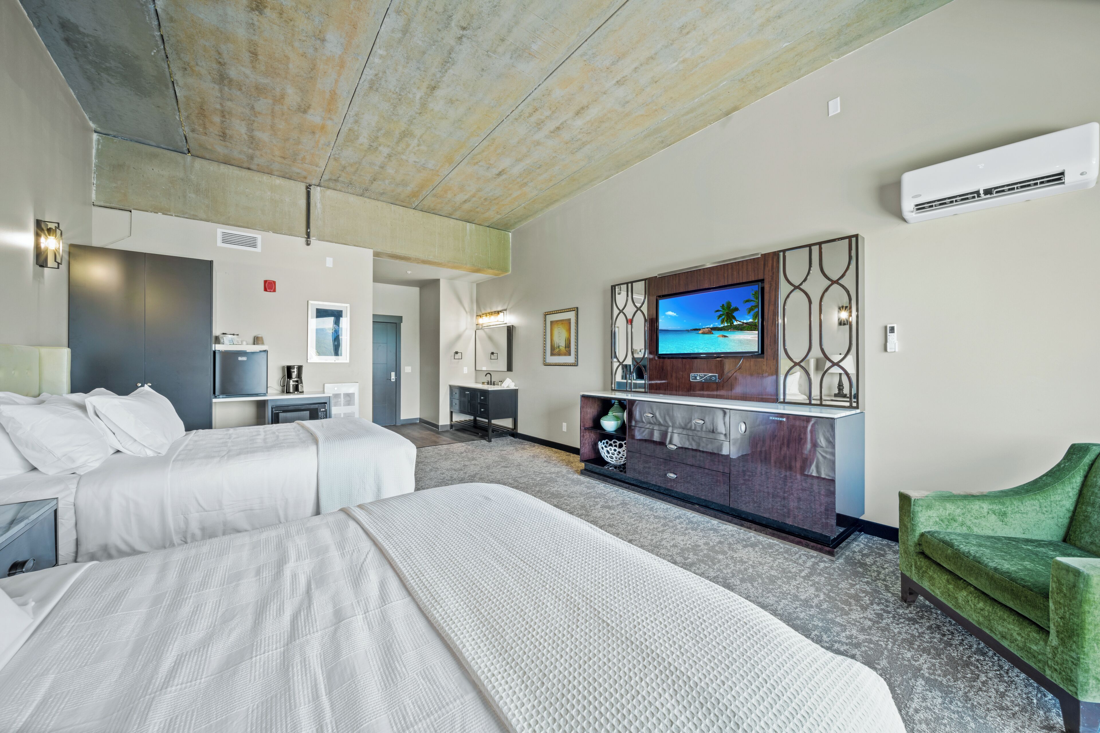 A hotel room with two beds, a TV, a minibar, and a green armchair.