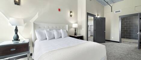 A hotel room with a large bed, two bedside tables with lamps, a modern ceiling, and a door leading to a bathroom.