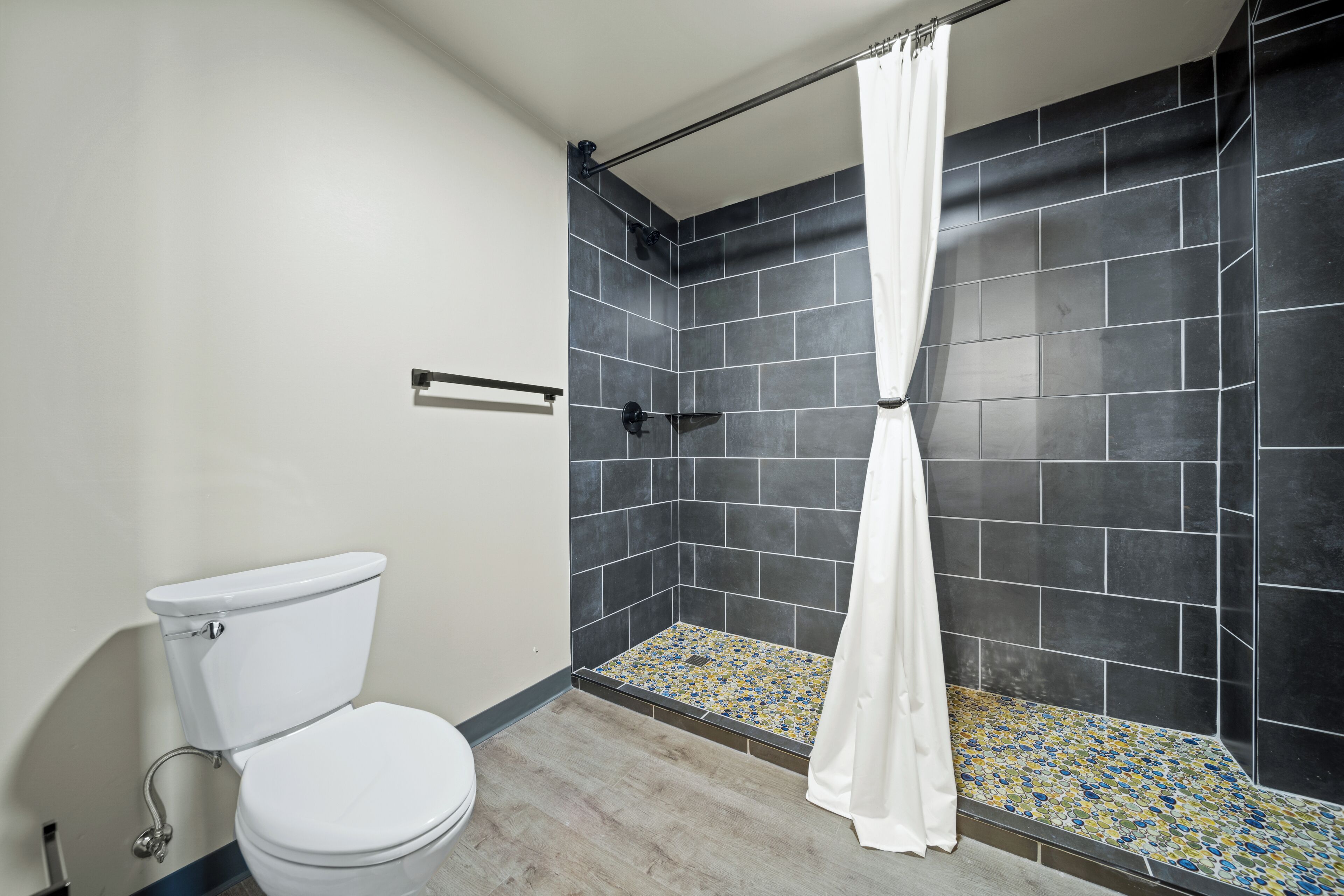 A bathroom with a white toilet, a shower with a black tiled wall, and a shower curtain.