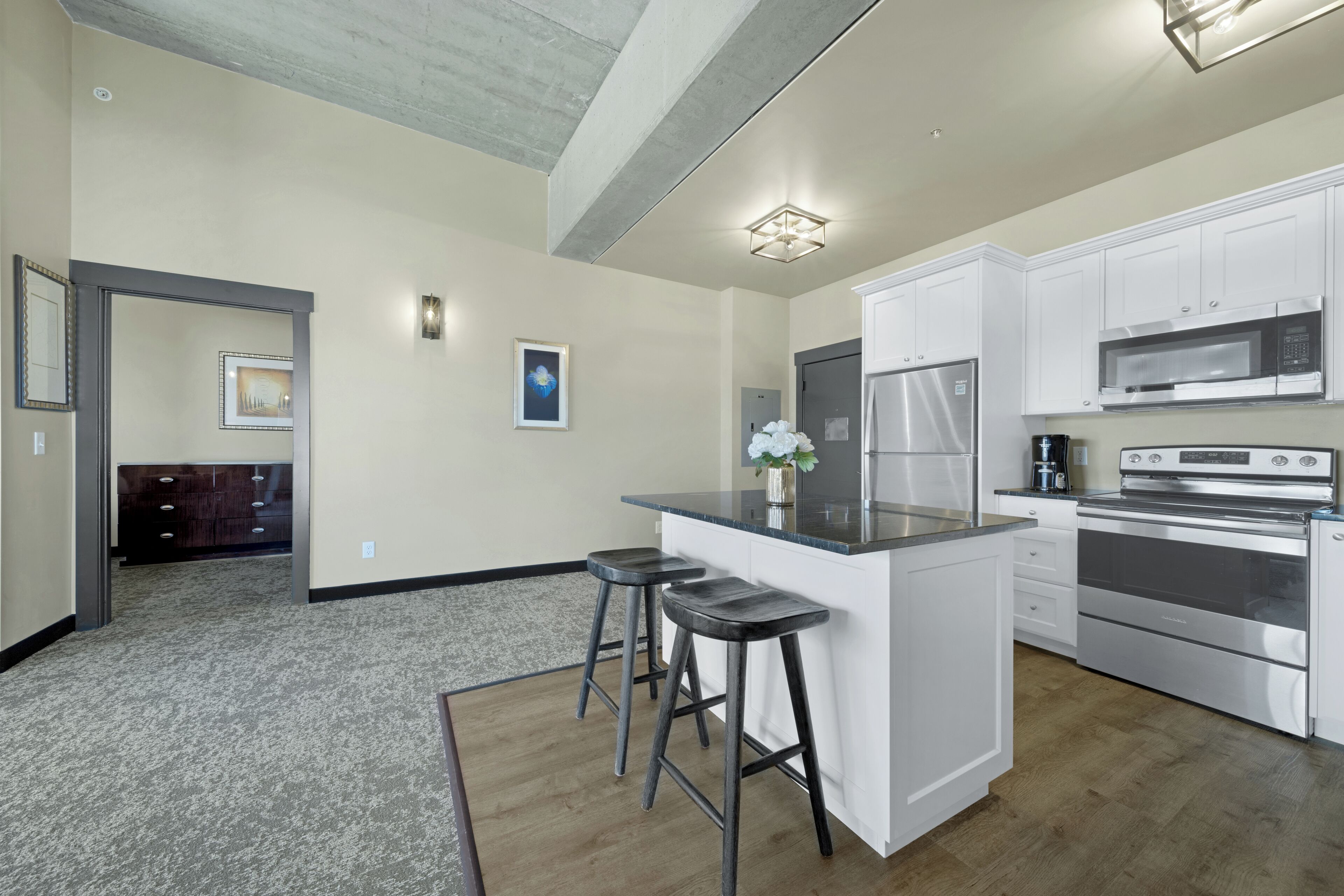 Una cocina moderna con gabinetes blancos, electrodomésticos de acero inoxidable y una isla central con taburetes.
