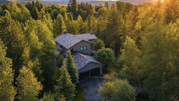 A house surrounded by dense forest with a clear view of the mountains in the background. - RMR: Lake Creek Cottage Home in The Aspens (Wilson)