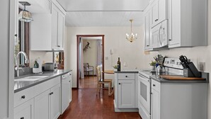 A modern kitchen with white cabinets, a wooden floor, a dining area with a table and chairs, and a chandelier. - RMR: Lake Creek Cottage Home in The Aspens (Wilson)
