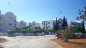 A residential area with modern buildings, a paved road, and parked cars.