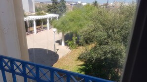A view from a balcony with a blue railing, overlooking a courtyard with a pergola, a lamp post, and dense greenery.