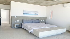 Une chambre à coucher moderne avec un grand lit, une tête de lit, une table de chevet et une petite étagère.