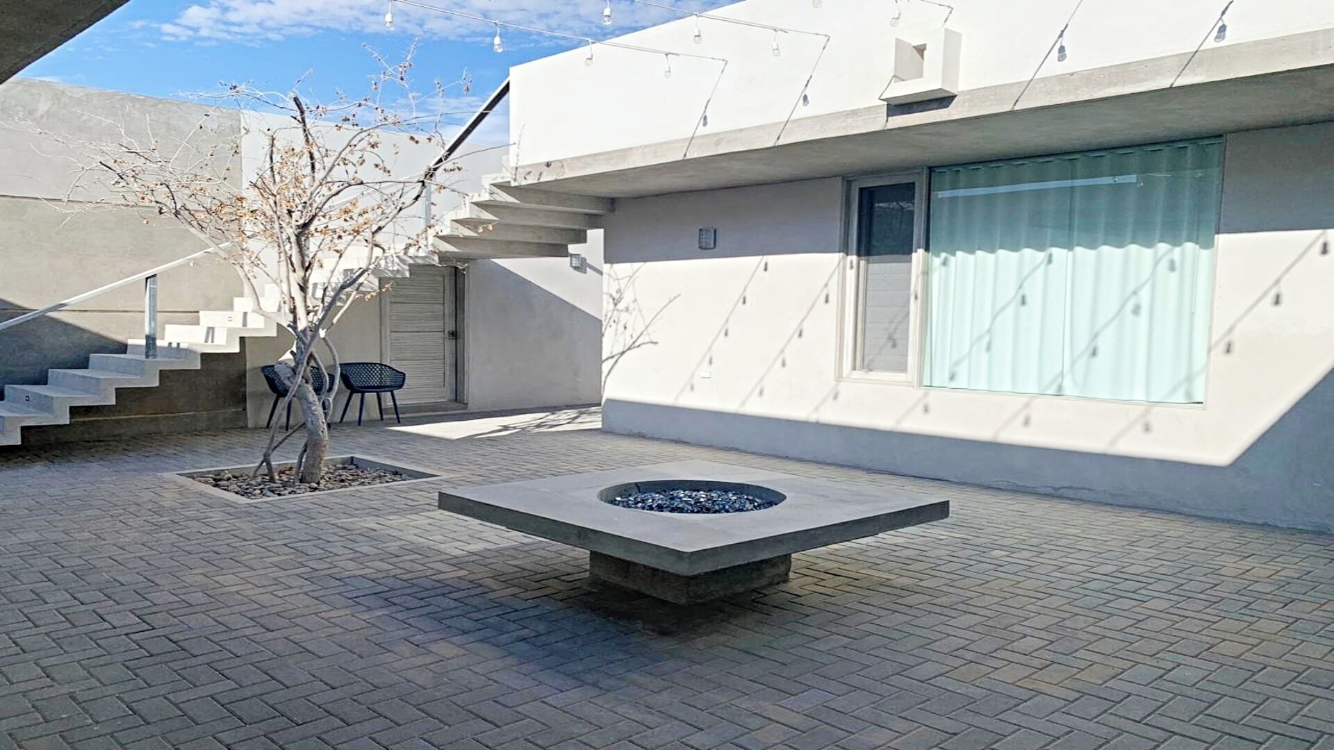 Un área exterior moderna con un hogar de fuego de concreto, una escalera y un árbol.
