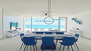 Un salon moderne avec une grande table à manger, des chaises bleues et une vue sur l’océan.