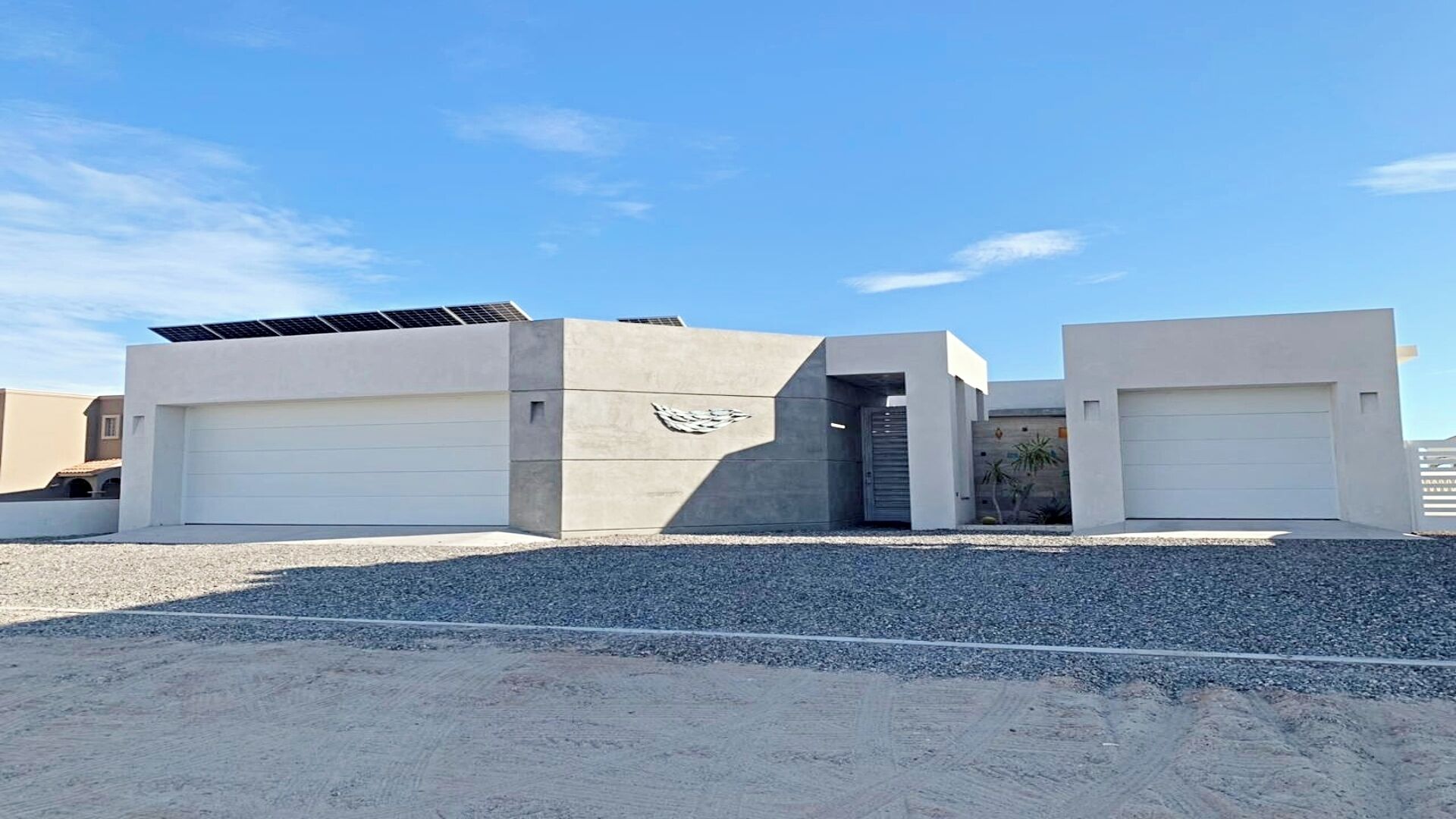 Un edificio moderno con dos puertas de garaje, un panel solar en el techo y fachada de hormigón.