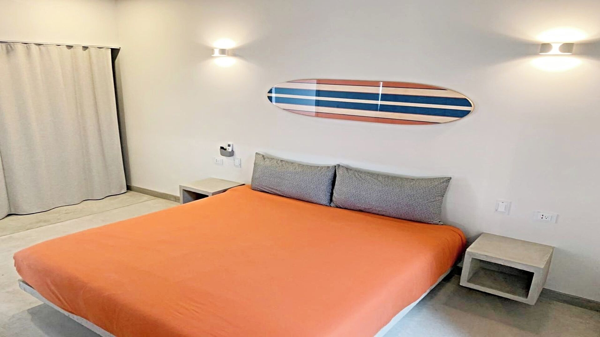 Une chambre d’hôtel avec un grand lit, deux tables de chevet, une décoration murale représentant une planche de surf et une fenêtre avec des rideaux.