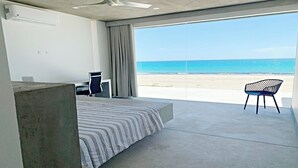 Habitación de hotel moderna con una cama grande, un escritorio y una silla. La habitación tiene vista a la playa y al océano.