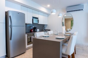 Uma cozinha moderna com micro-ondas embutido, frigorífico de aço inoxidável e área de refeições com mesa posta para quatro pessoas.