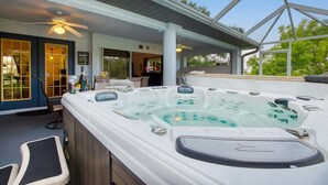 Un espace avec un bain à remous, doté d’un patio couvert, d’un ventilateur de plafond et offrant une vue sur le jardin arrière.