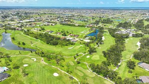 Vue aérienne d’un parcours de golf comportant plusieurs trous, avec des plans d’eau et des zones résidentielles en arrière-plan.