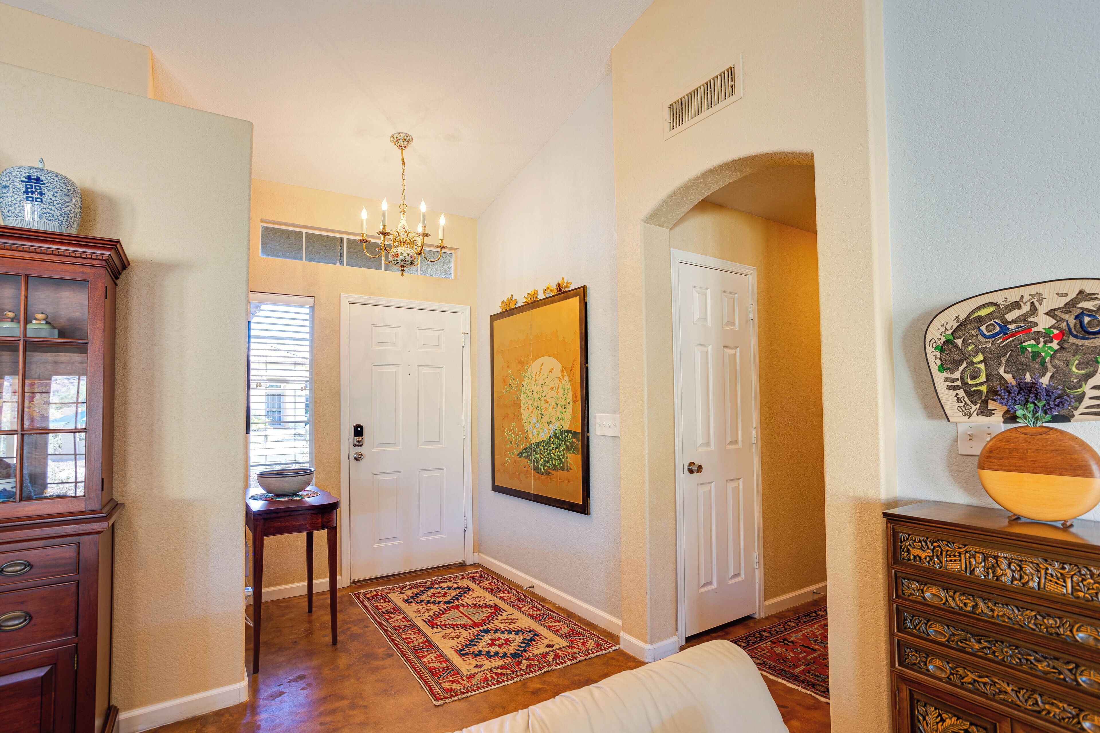 A hallway with a chandelier, a framed artwork, and a wooden cabinet.