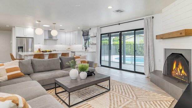 A modern living room with a sofa, coffee table, fireplace, and a view of a swimming pool through large glass doors. - White Agate by Avantstay Pool + Spa + Putting Green Playground + Outdoor Dining Minutes to Kierland (Scottsdale)