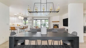 A modern dining area with a large table, chairs, a fireplace, and a kitchen in the background. - White Agate by Avantstay Pool + Spa + Putting Green Playground + Outdoor Dining Minutes to Kierland (Scottsdale)